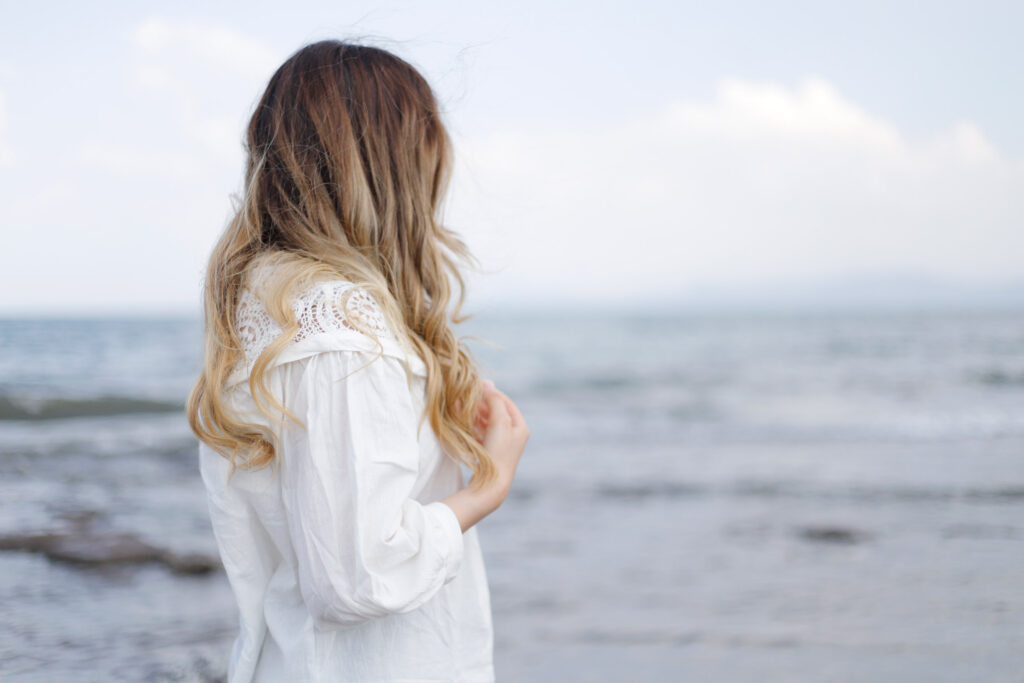 A stressed-out woman on the beach glances out at the ocean deep in thought.